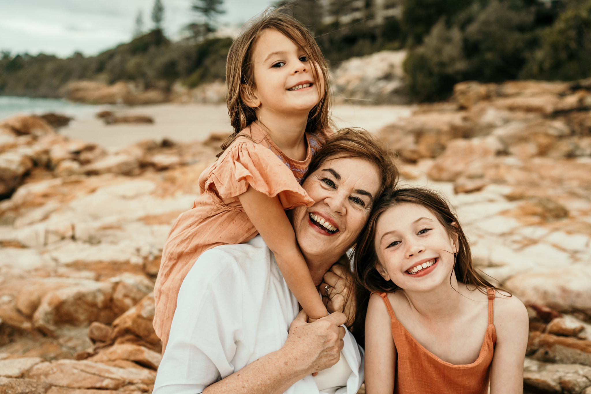 Smiling mother with her two daughters posing on a rocky beach.