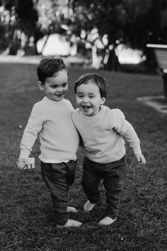 Two smiling young children walk arm in arm across a grassy area.
