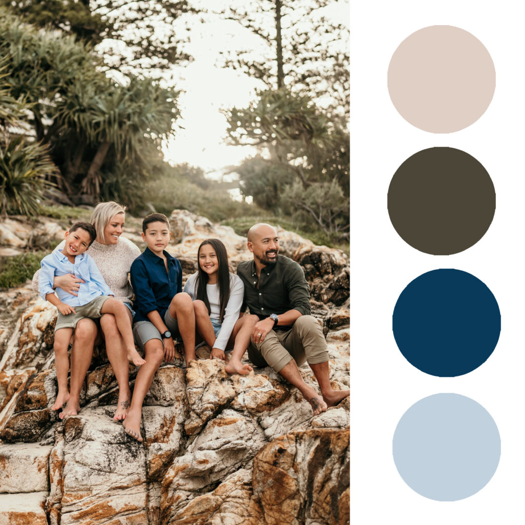A family of five sits together on a rocky outcrop outdoors, smiling at the camera.